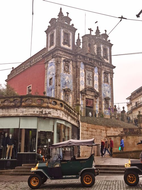 Free A bustling street scene featuring the ornate facade of a baroque church in Porto, Portugal, with people and vintage cars in view. Stock Photo