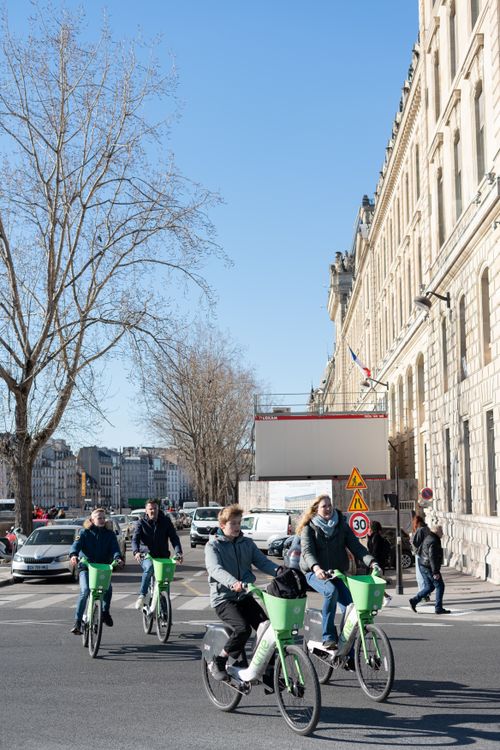 Free Group of cyclists ride green bikes on sunny day in Paris, France, promoting sustainable urban transport. Stock Photo