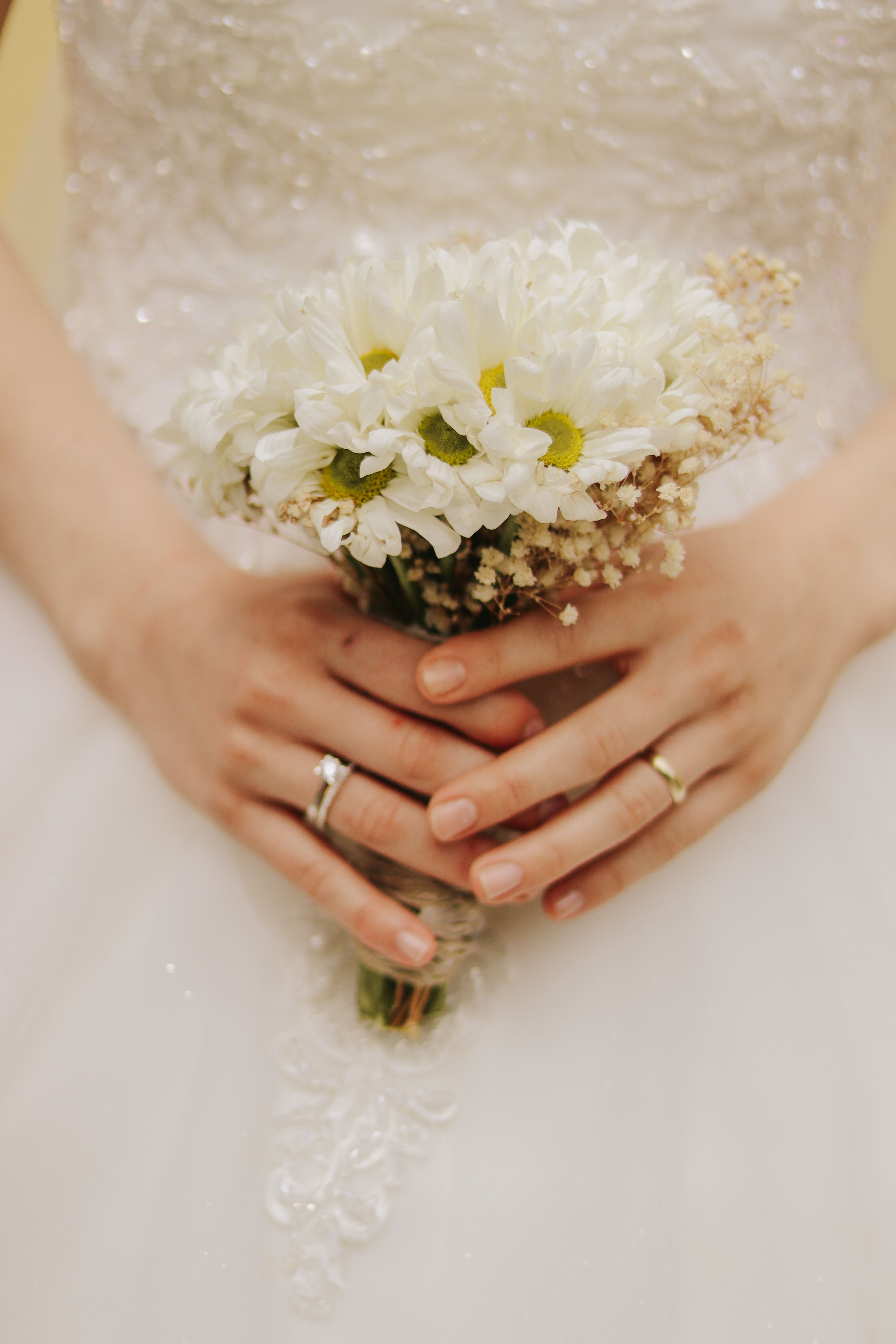 A detailed close-up of a bride holding a white floral bouquet against an elegant wedding dress.