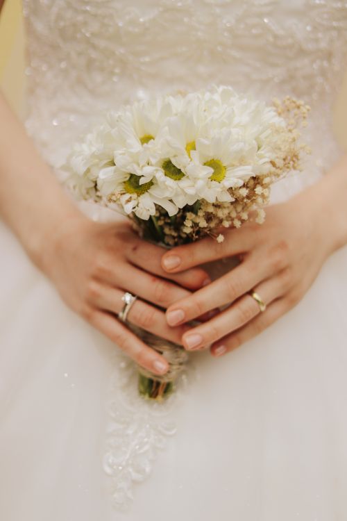 Free A detailed close-up of a bride holding a white floral bouquet against an elegant wedding dress. Stock Photo