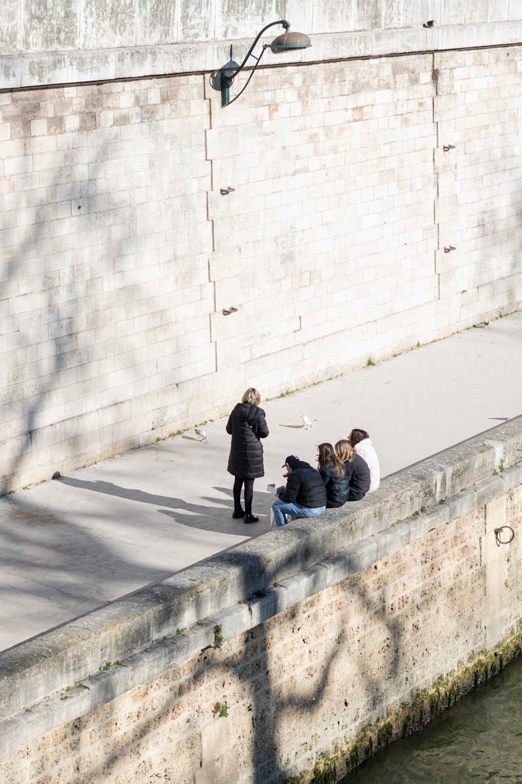 Group Of People Resting On Footpath On Riverbank