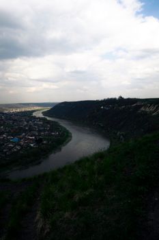 Aerial view of a winding river alongside a town under a cloudy sky.