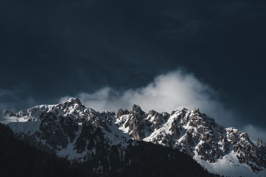 Stunning snowy mountain peaks under a dramatic dark sky at twilight, showcasing natural beauty.