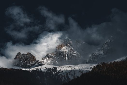Stunning view of snow-covered mountains with dramatic clouds and dense forest below.