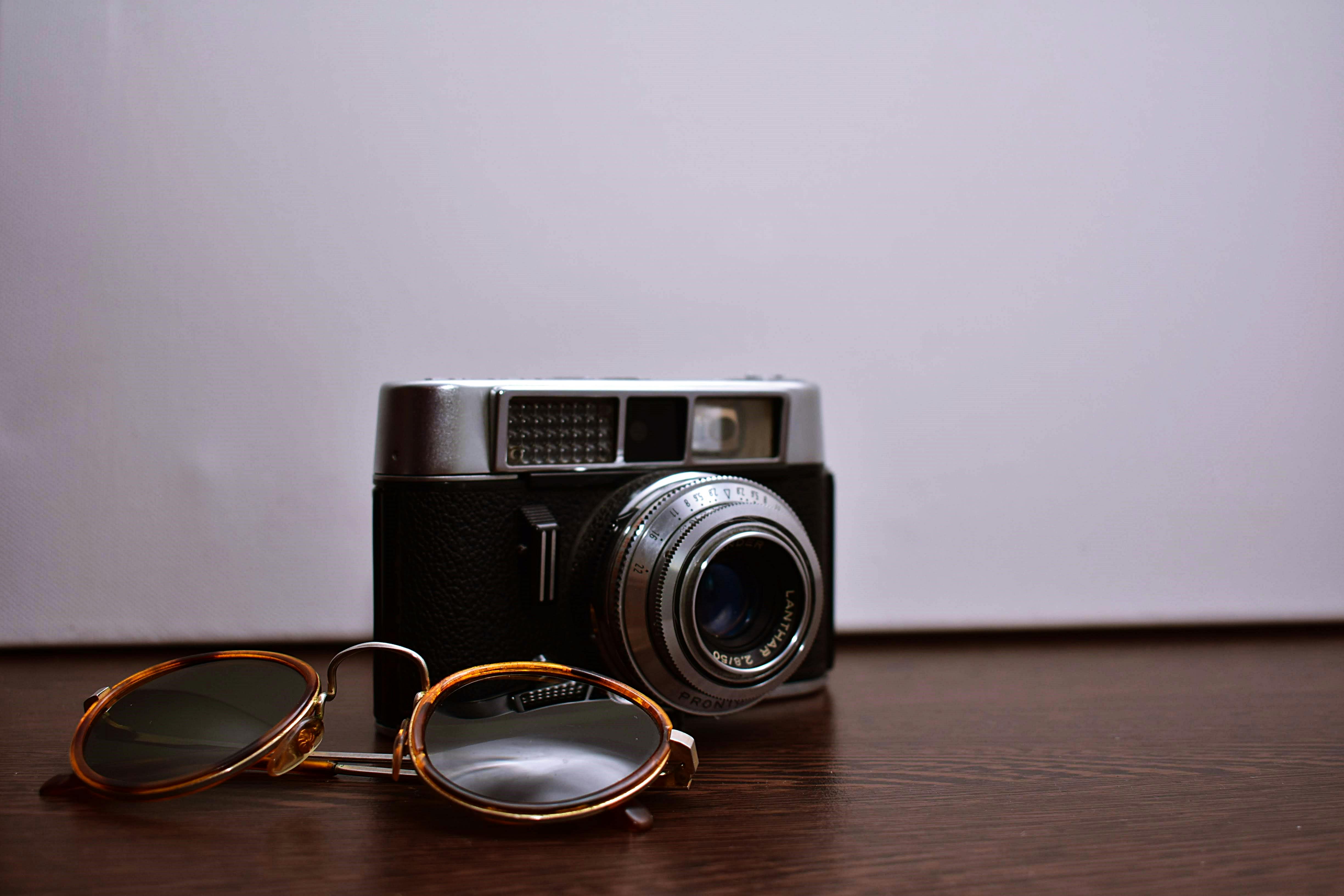 木桌上，一台经典的胶片相机与太阳镜的特写，展现出复古风格