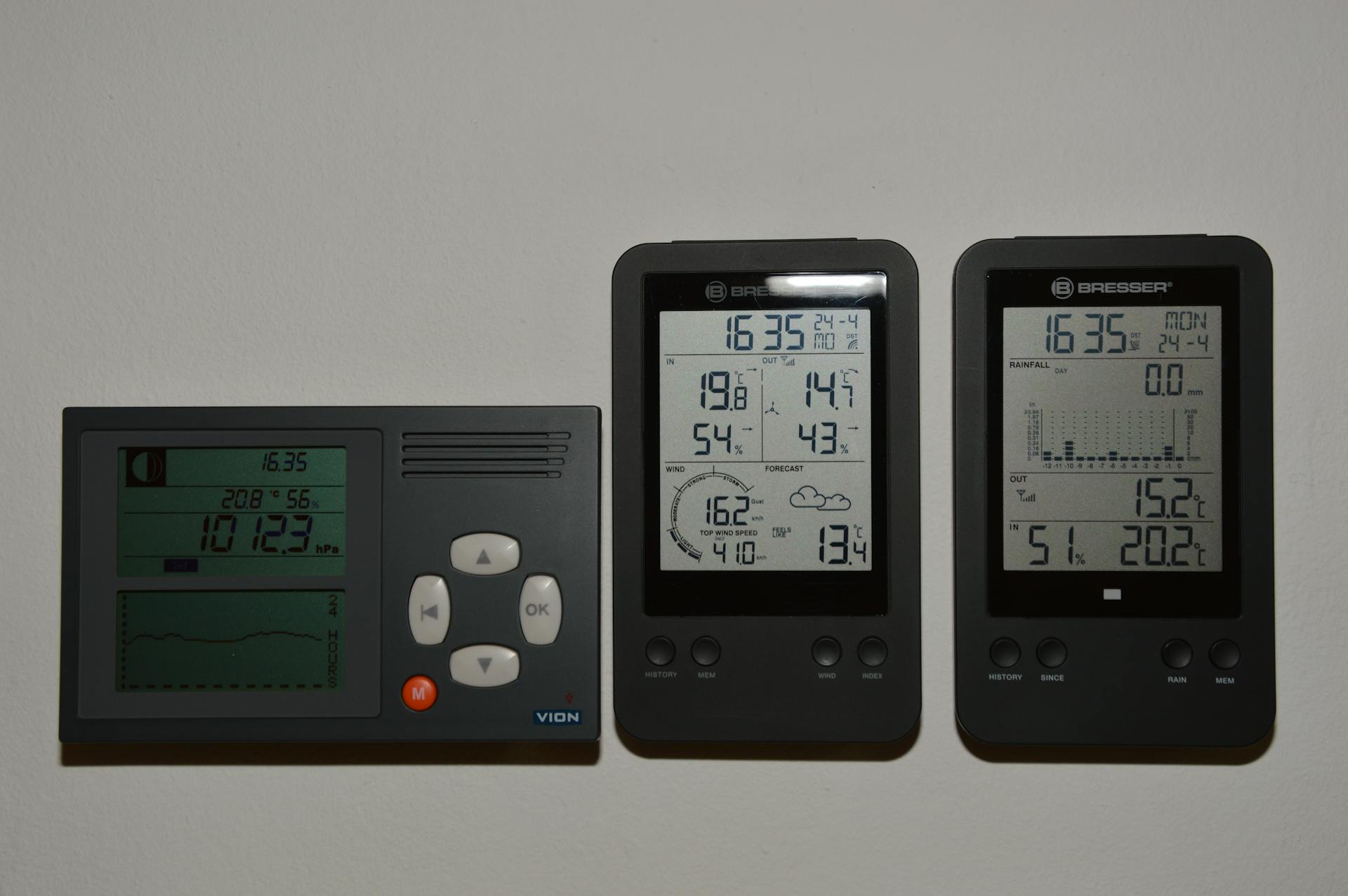 Multiple digital weather monitors on a wall displaying temperature and pressure.