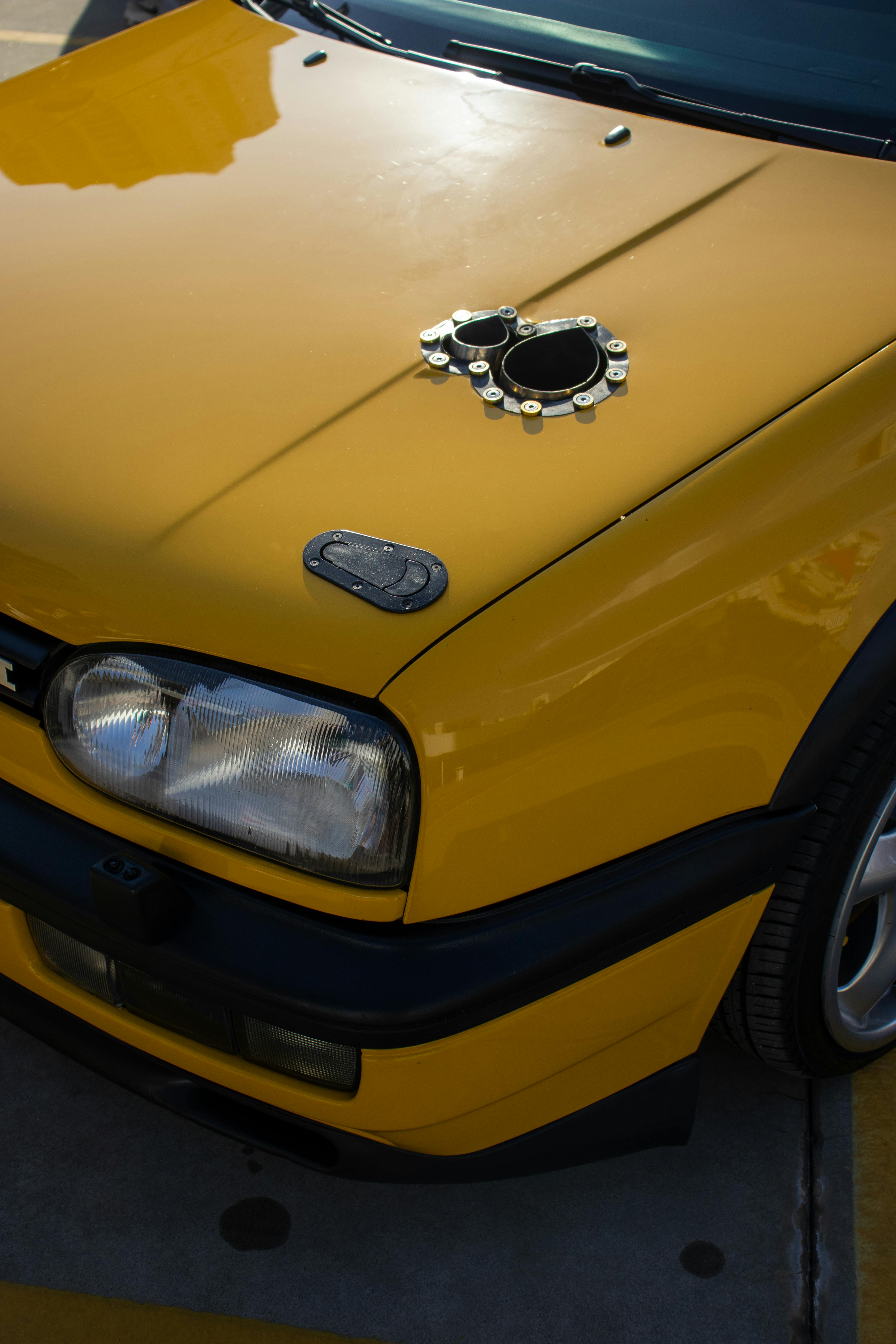 Yellow car hood featuring metal fixture, highlighting automotive design.