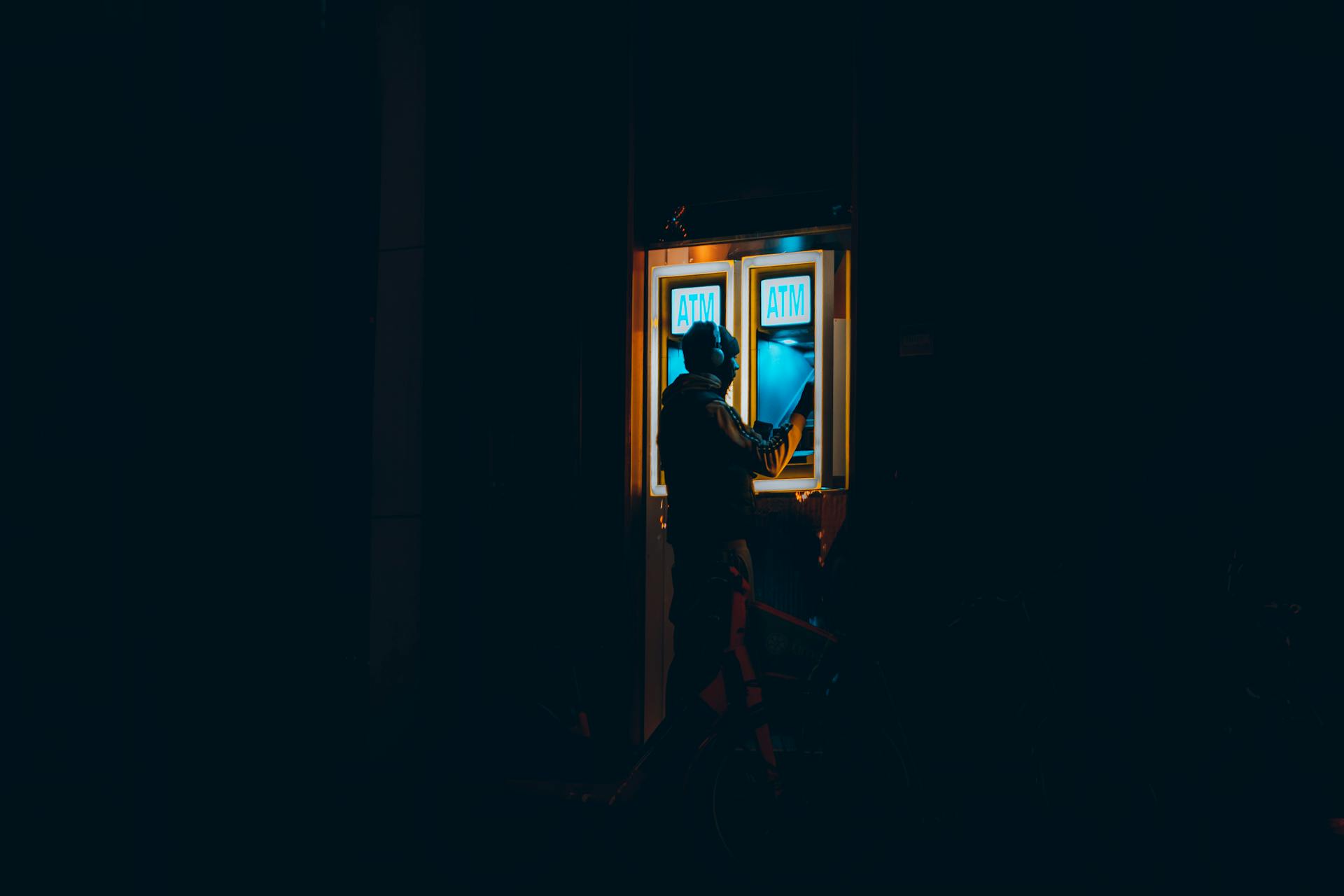 A man interacting with an ATM at night in a dark urban environment in Rotterdam.