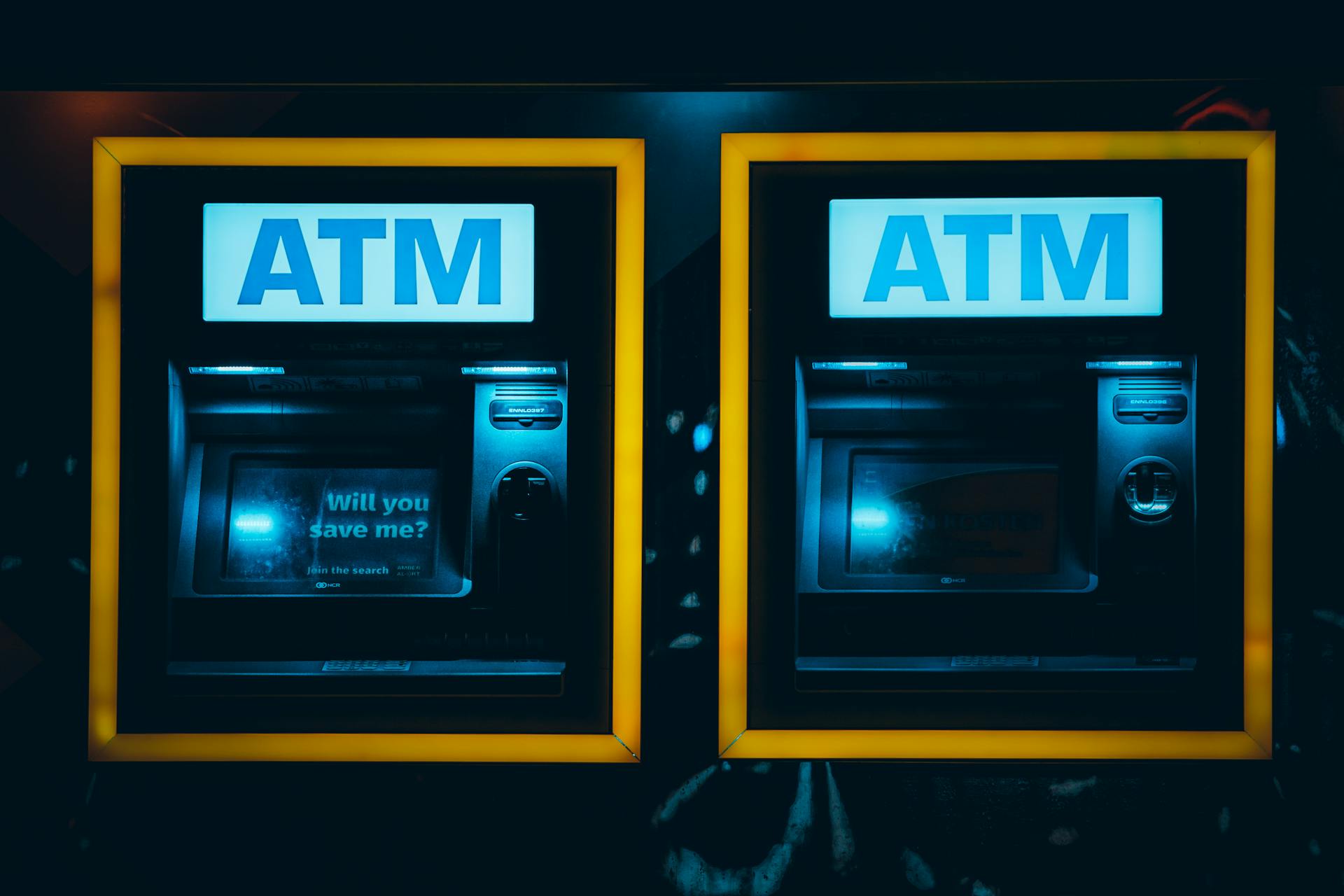 Two illuminated ATMs in a dark urban setting in Rotterdam, Netherlands.