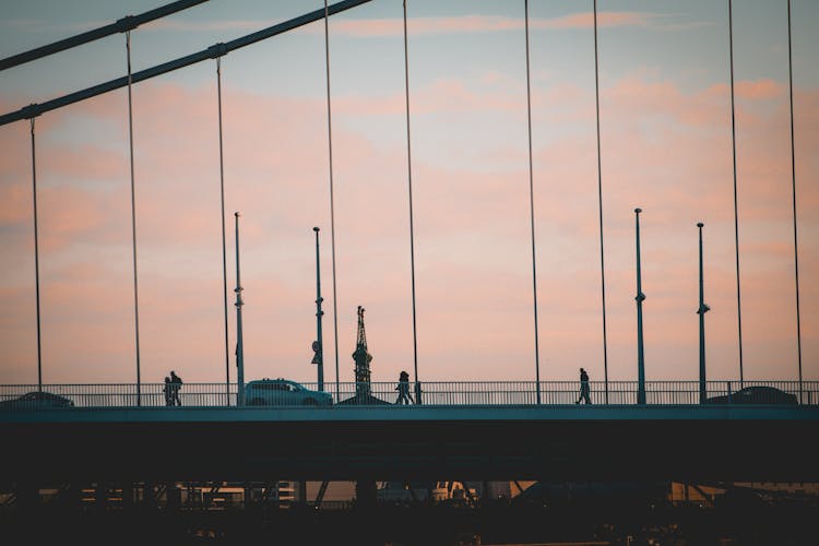 Silhouette Of People Walking On A Bridge At Dusk 