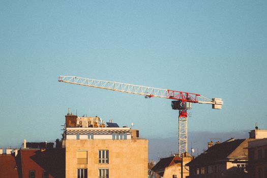 Construction crane towering over Budapest cityscape under a warm sunset sky.
