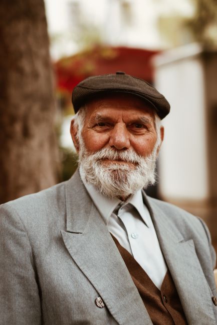 Elegant elderly man with a beard and hat, exuding wisdom and warmth in an outdoor setting.