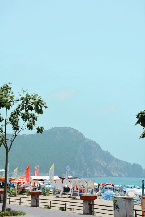 Free Vibrant beach with mountains in the background, clear sky, and colorful umbrellas. Stock Photo