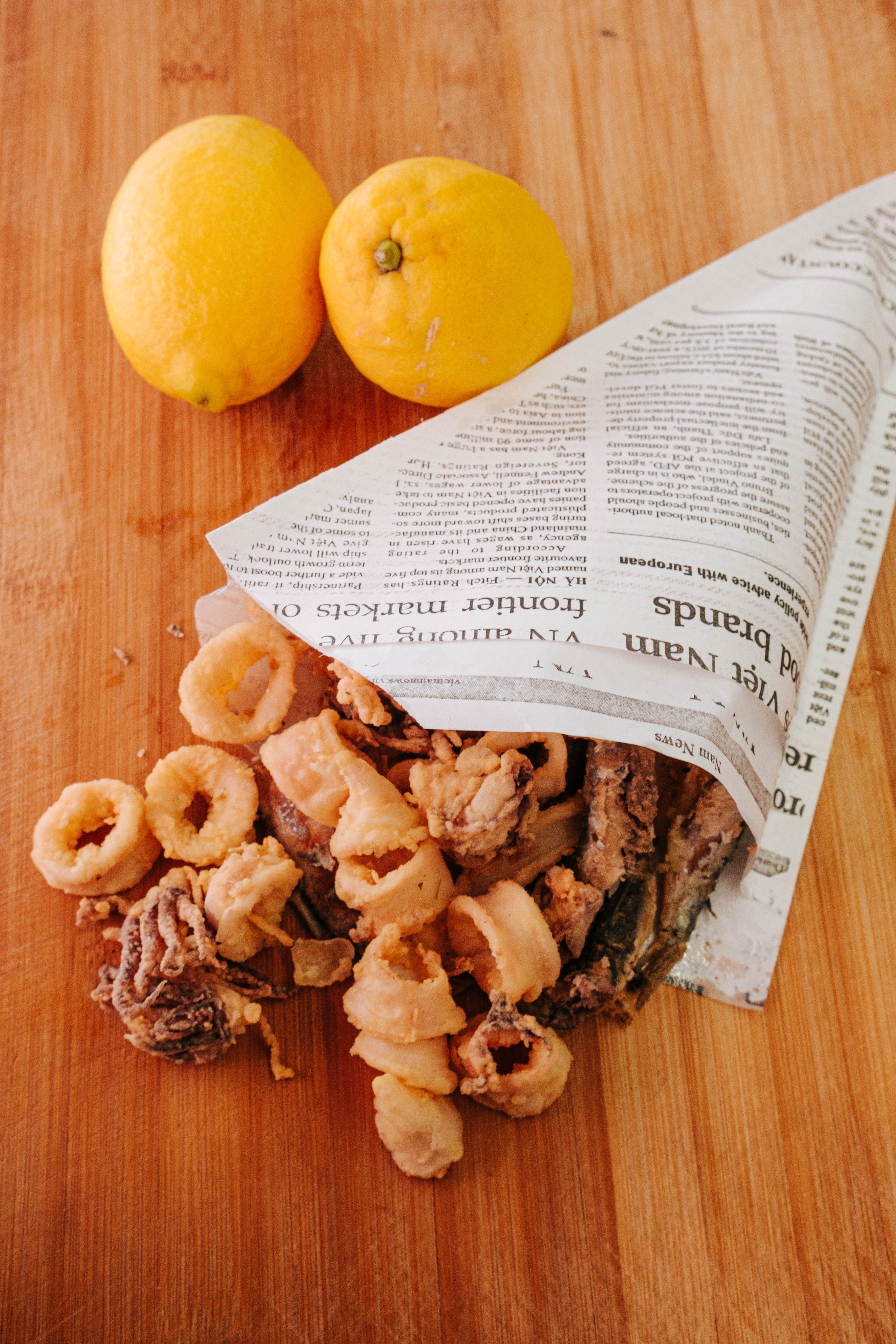 Tasty seafood snack of fried calamari with fresh lemons on a wooden surface.