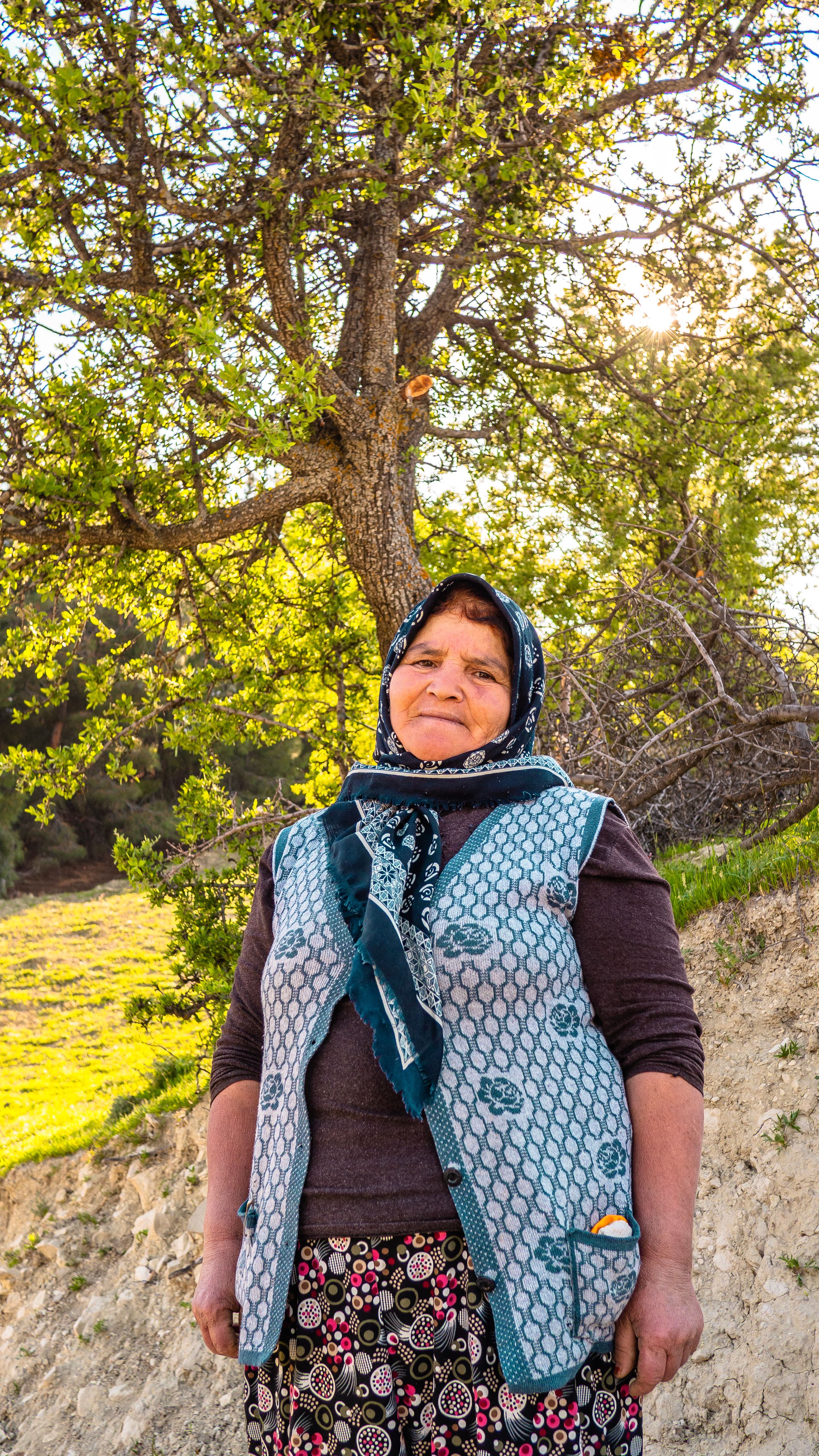 A cheerful elderly woman enjoying a sunny day in a park with lush trees.