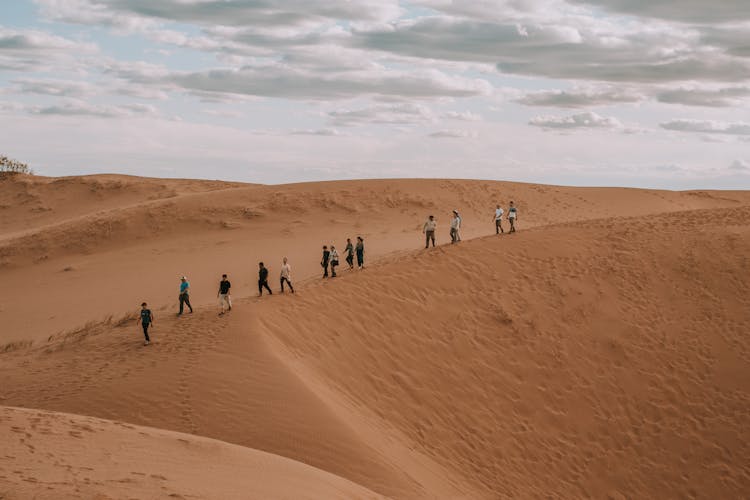 Group Of People Walking On A Dune In The Desert