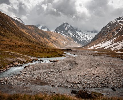 Majestic view of Obergurgl Alps with snow-capped peaks and a meandering stream.