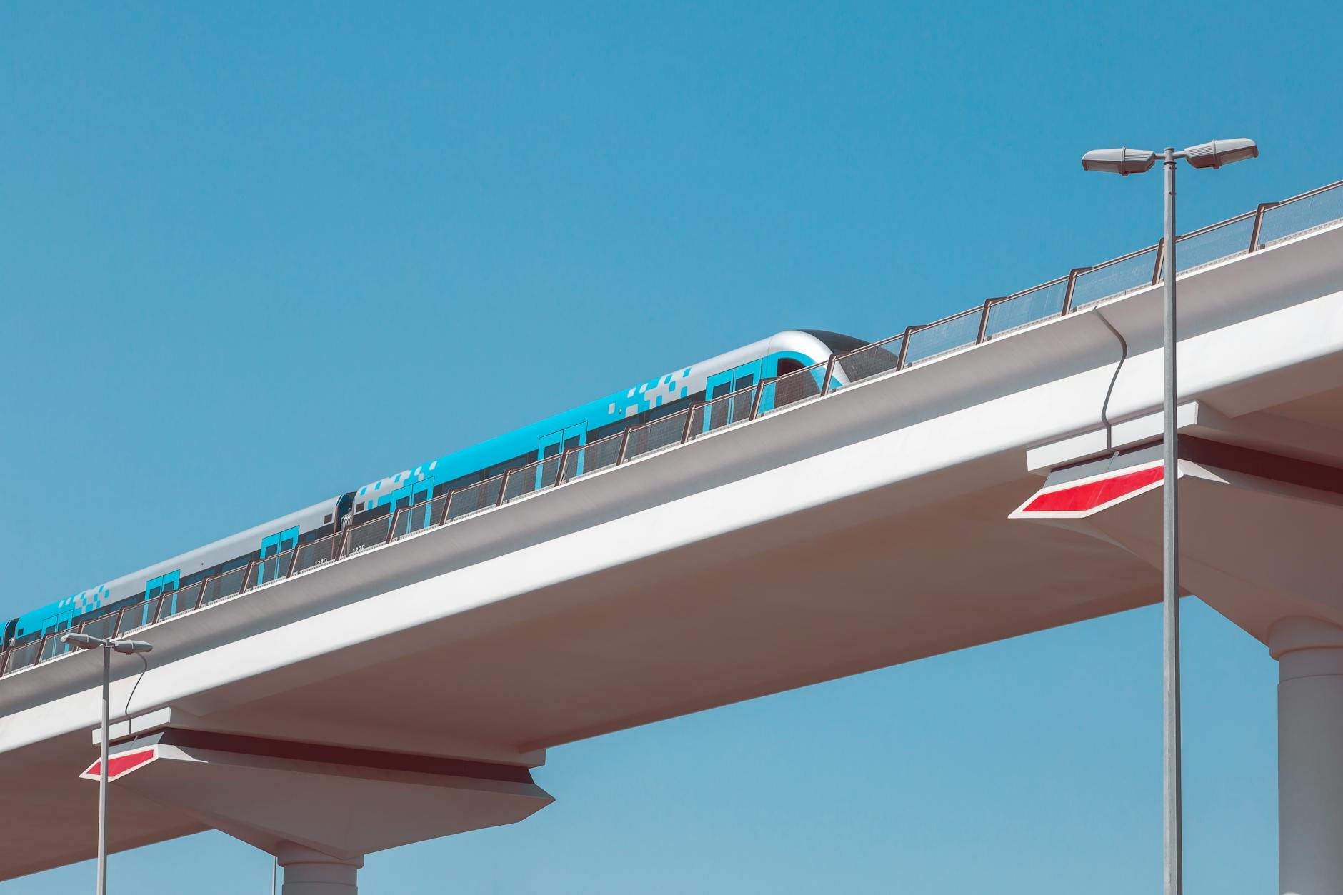 A sleek metro train travels on an elevated track against a blue sky in Dubai.