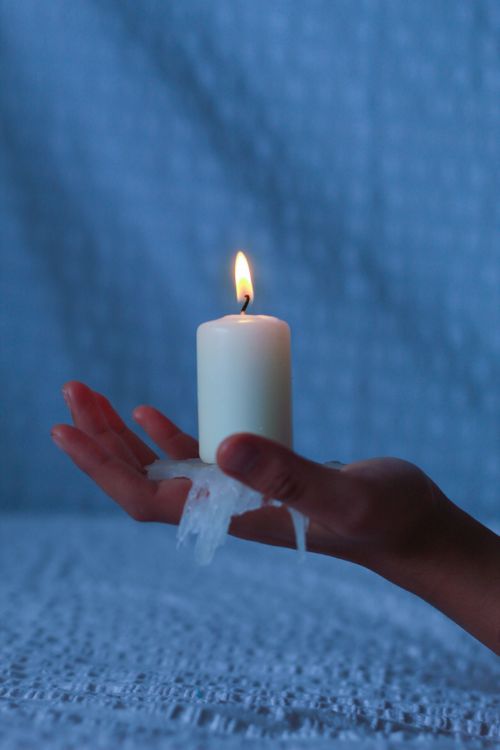 Free A hand holding a burning candle against a textured blue backdrop. Stock Photo