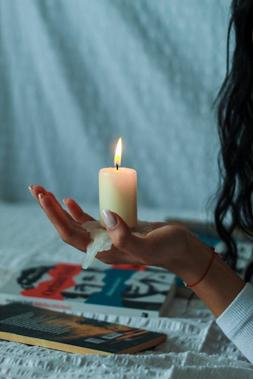 Burning Candle Melting in a Woman Hand over Books