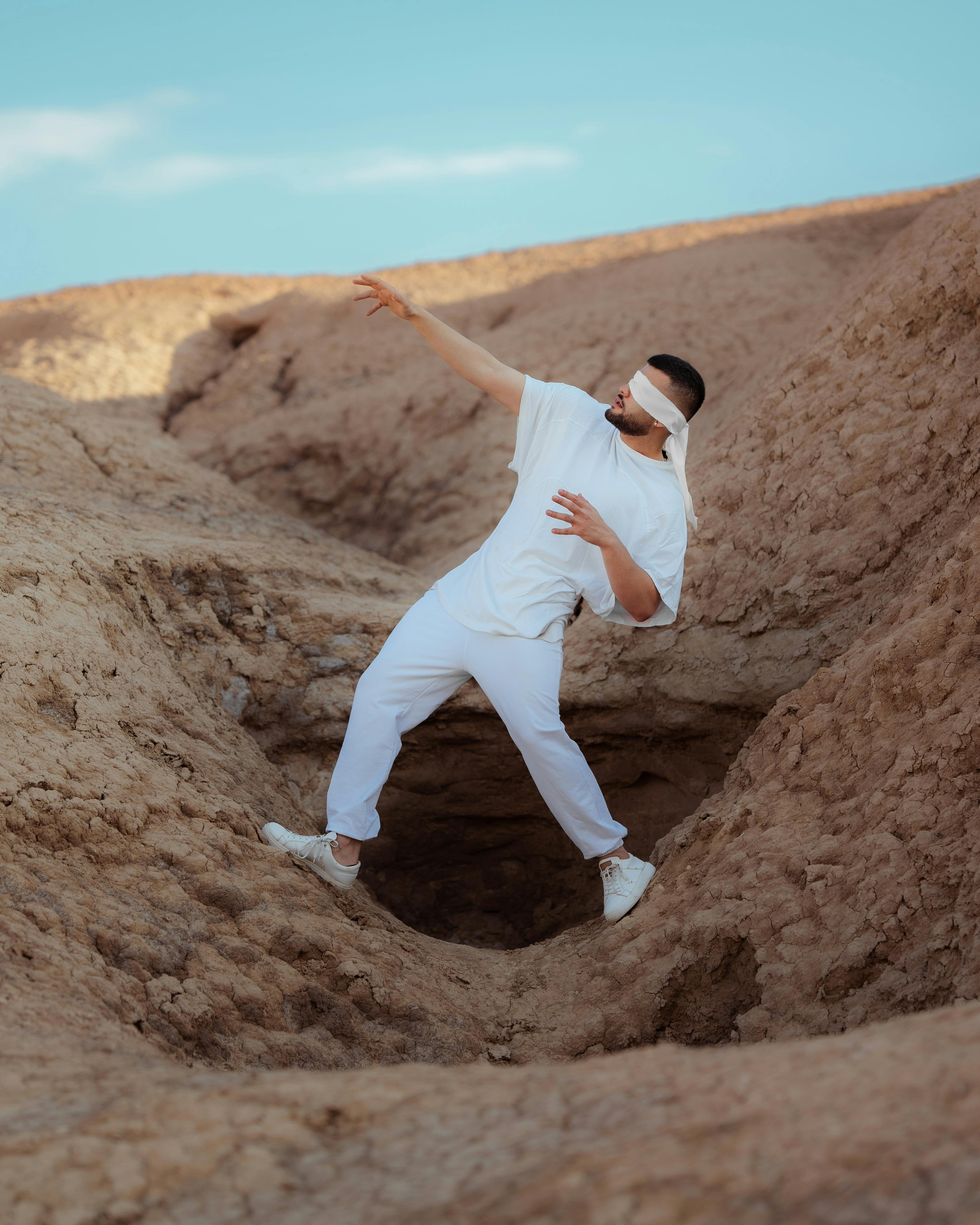 blindfolded man on the desert standing in a straddle position over the hole