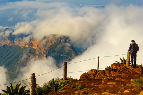 Free A lone man stands on a rugged mountain edge surrounded by clouds, capturing nature's beauty. Stock Photo