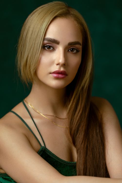 Free Stunning portrait of a woman with long blonde hair against a green background. Stock Photo