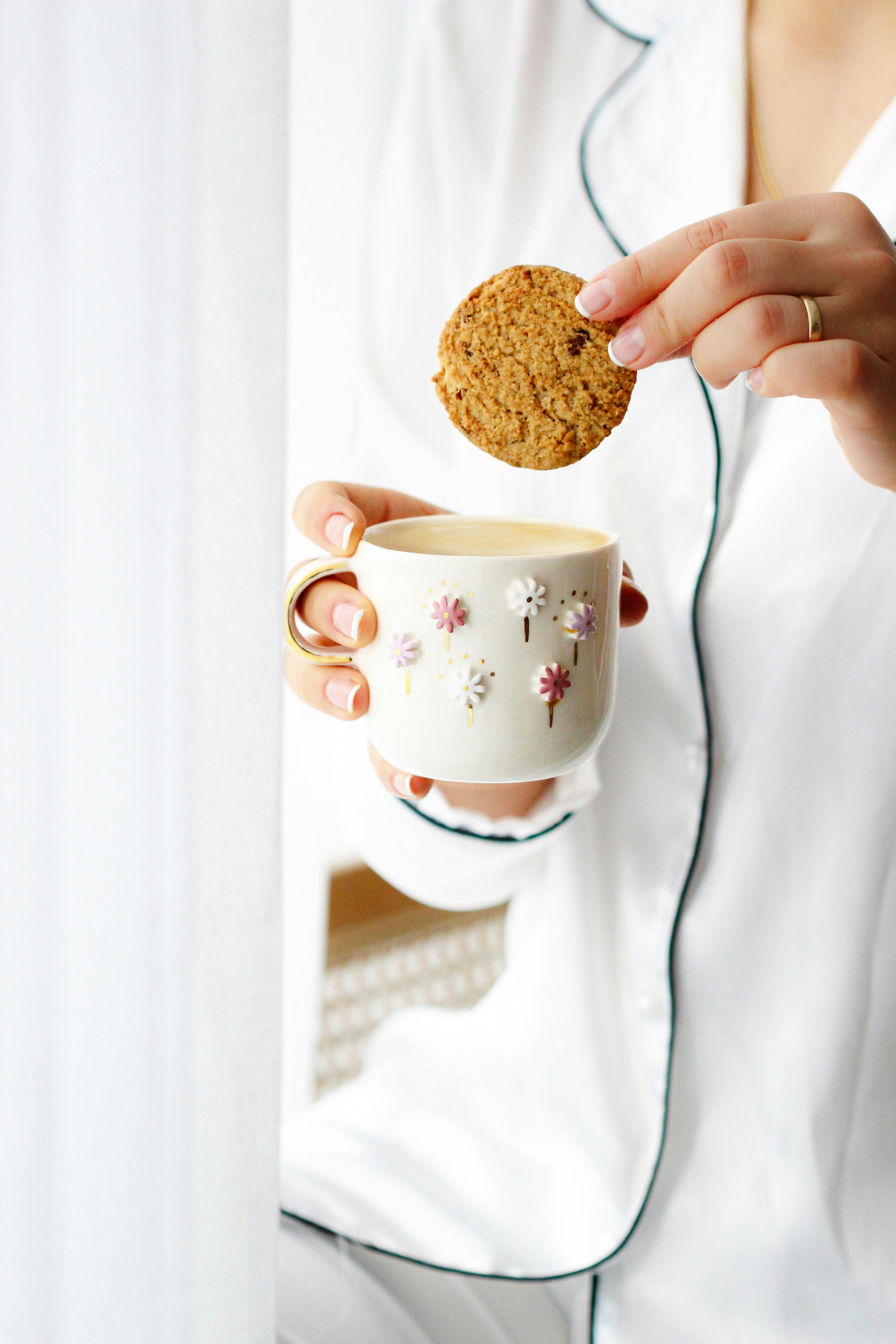 A relaxing morning moment with coffee and a cookie in minimalist white pajamas and floral mug.