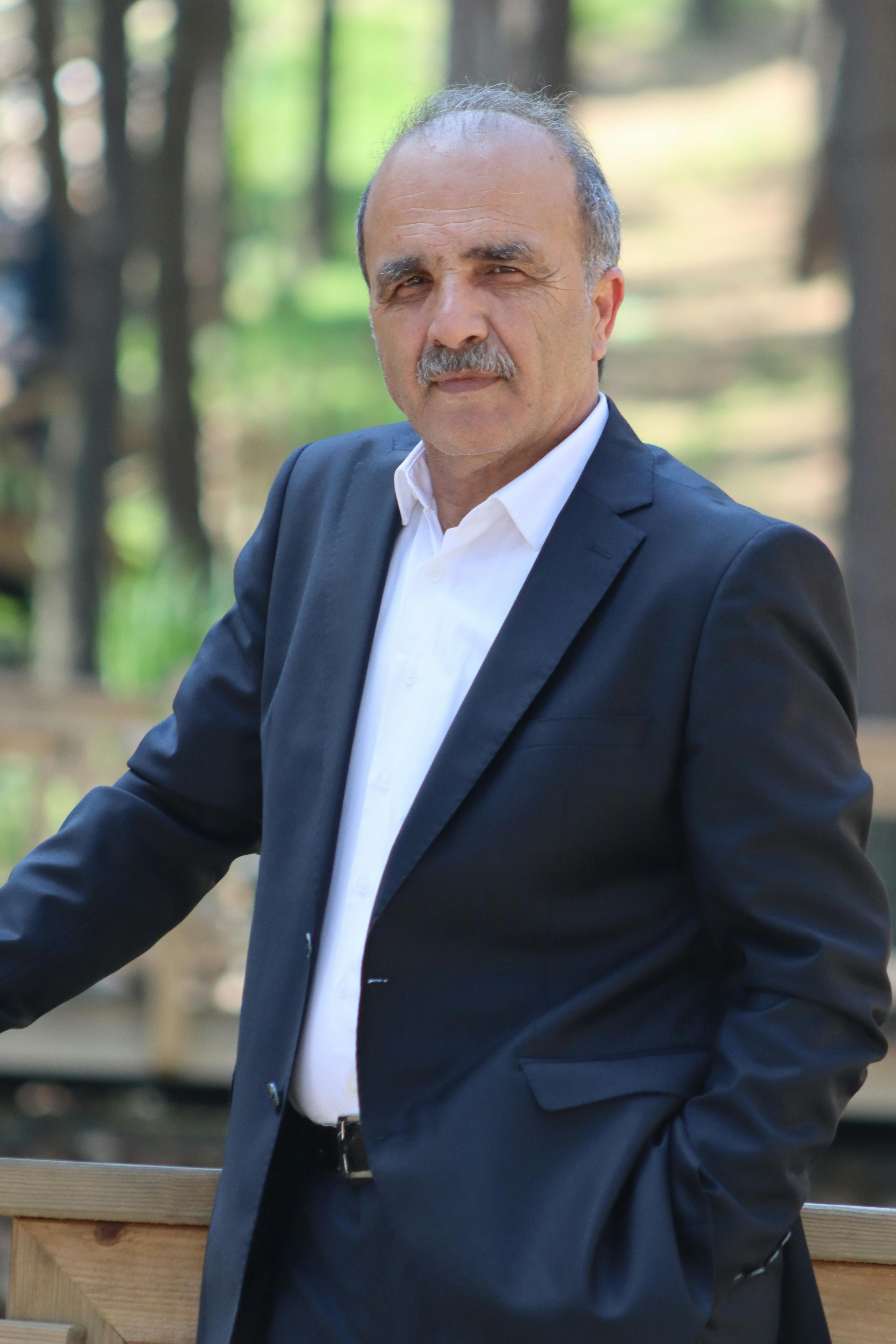 Senior man in a formal suit posing outdoors in a forest setting, exuding confidence and style.