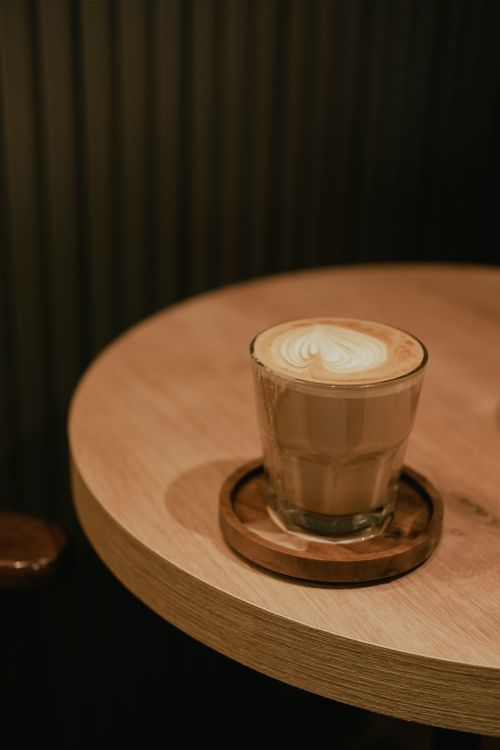 Free A beautifully crafted cappuccino on a wooden table in a warm, dimly-lit coffee shop. Stock Photo