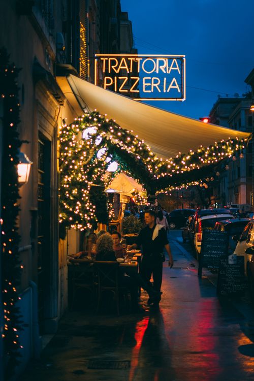 Free Inviting street view of a Trattoria Pizzeria with twinkling lights on a lively night. Stock Photo
