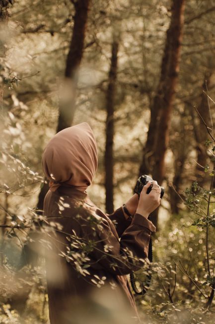 A woman in a hijab photography in a serene forest setting.