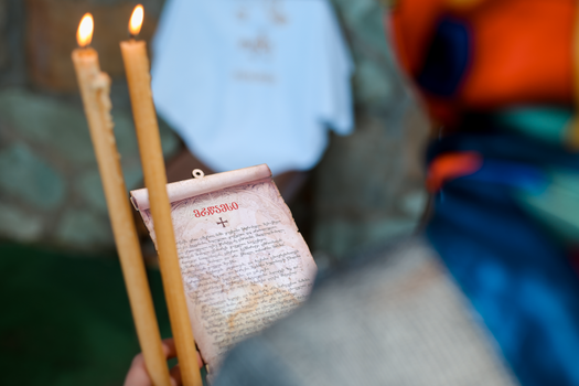 Close-up of a religious ceremony with lit candles and an Orthodox prayer scroll.