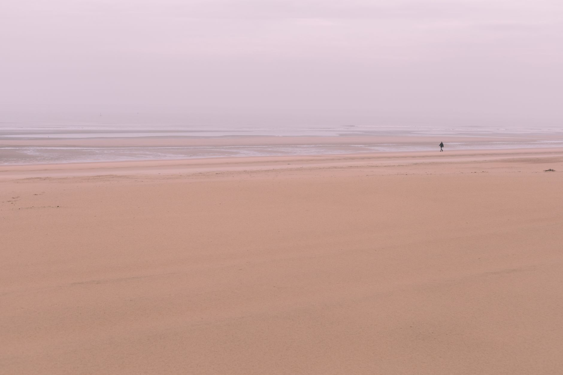 A lone figure walks on the misty beach of Oostende, Belgium at sunrise.