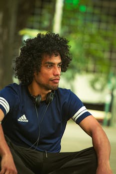 Portrait of a man in Adidas sportswear seated outdoors, wearing headphones.