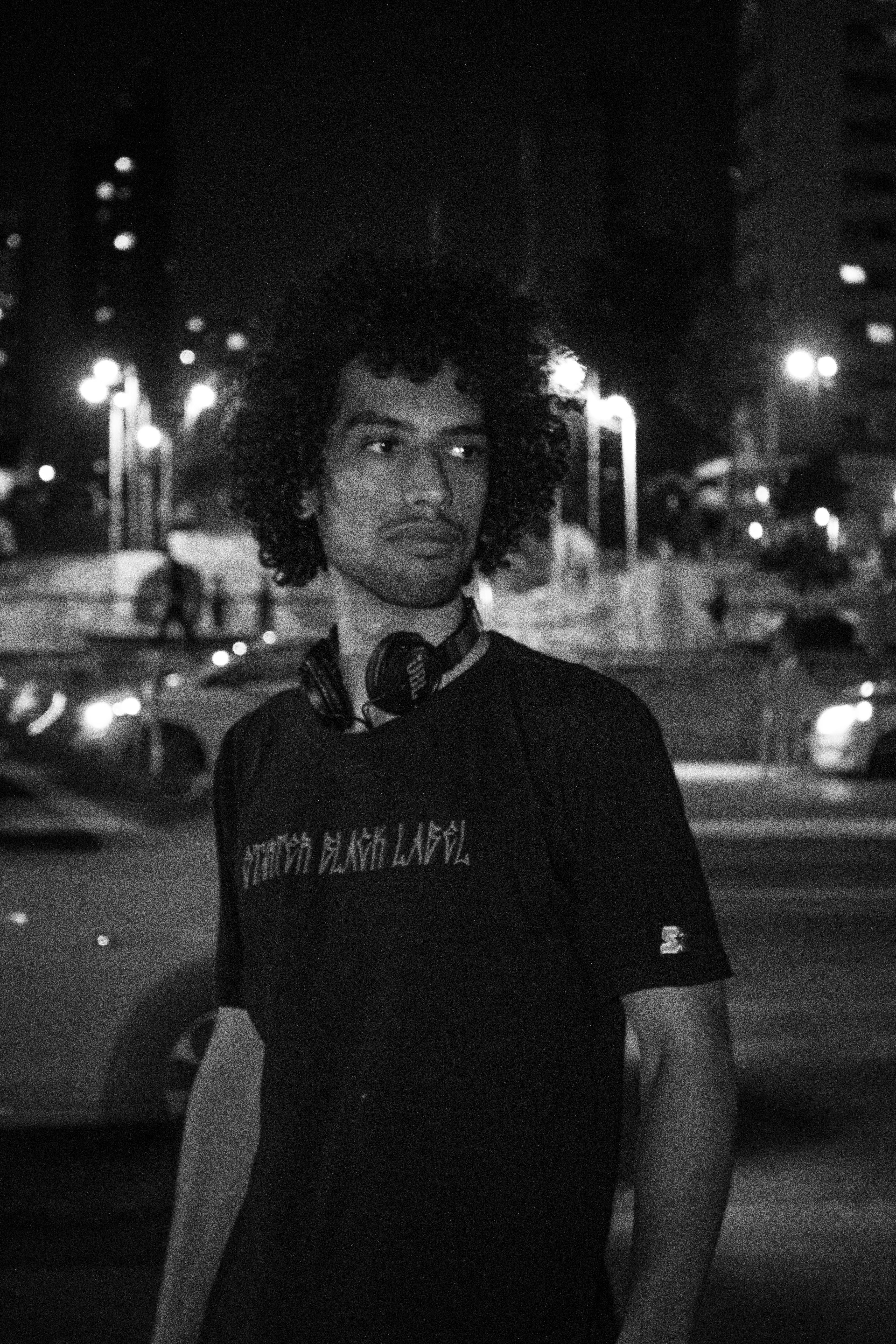 Black and white portrait of a man with curly hair and headphones in an urban night setting.