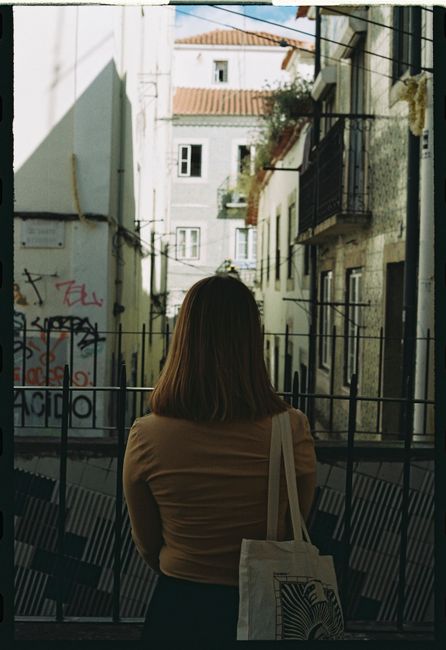 Back view of a woman with a shopping bag standing in a narrow alley in Lisbon, Portugal.