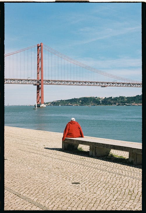 Tourist Sitting on the Tejo Promenade Near 25 de Abril Bridge in Lisbon