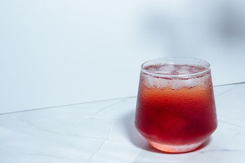 Free Chilled red drink in a short glass with ice, set on a marble surface, evoking freshness. Stock Photo
