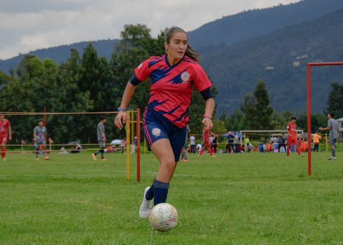 Focused young female soccer player dribbling on a lush green field during a daytime match.