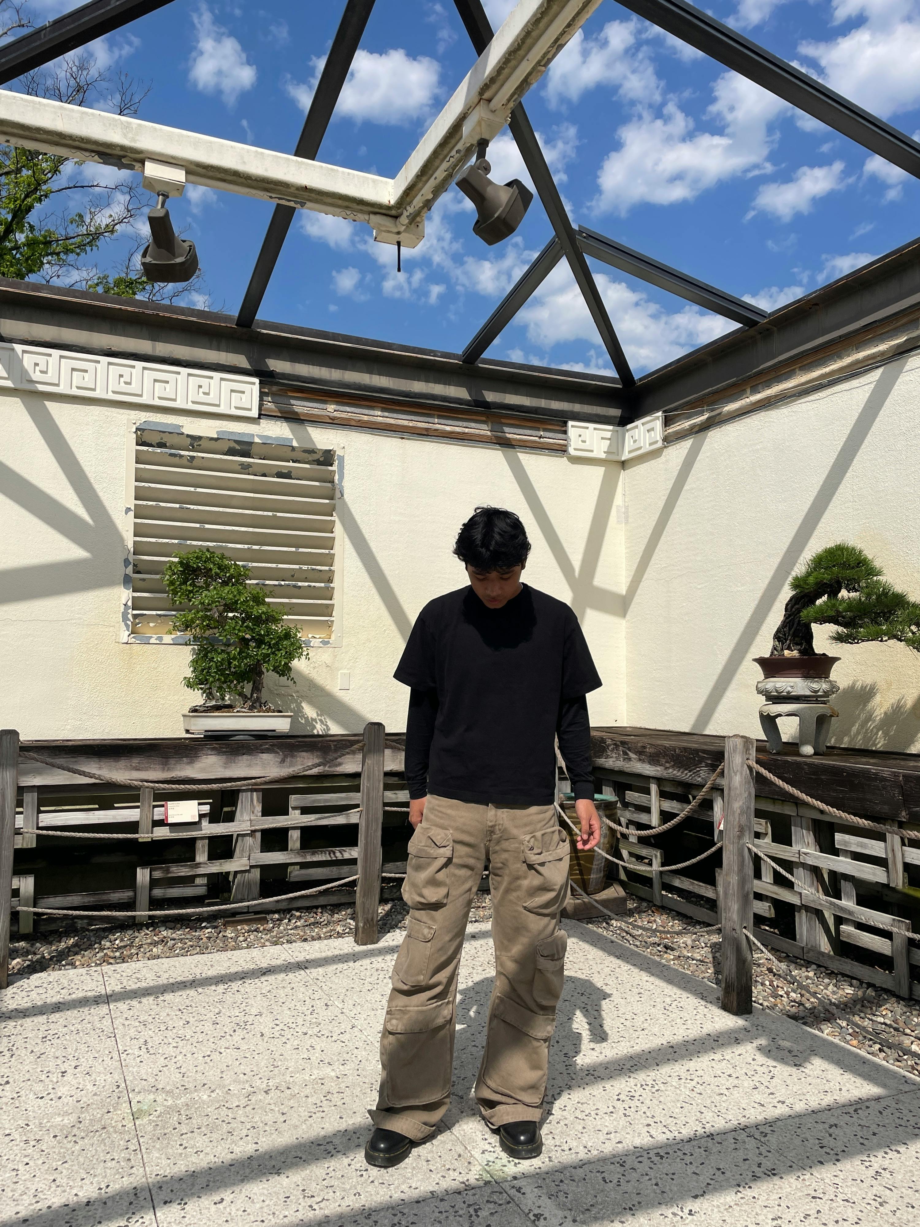 A person stands in a glass-roofed atrium with two bonsai trees visible on either side