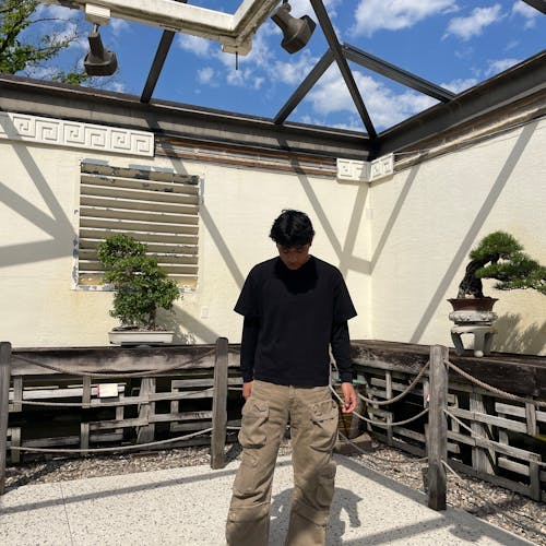 A person stands in a glass-roofed atrium with two bonsai trees visible on either side