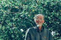 白天，一位老人戴着眼镜，在郁郁葱葱的花园里微笑着