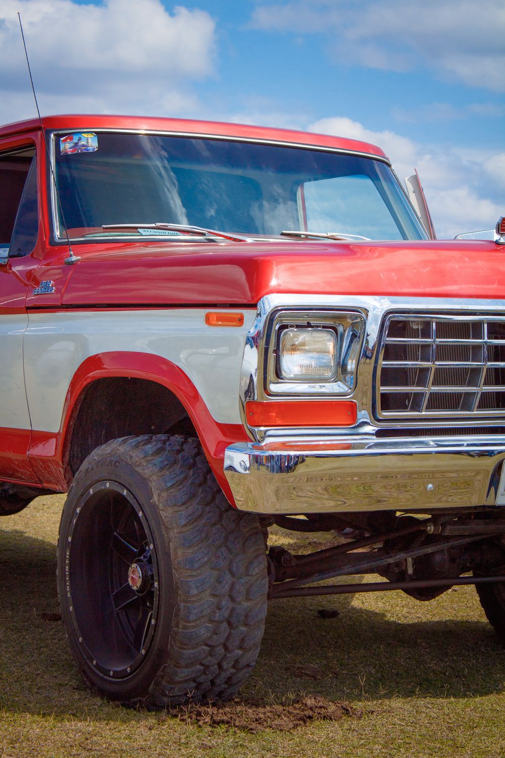 Red and white classic pickup with a suspension lift and mud tires