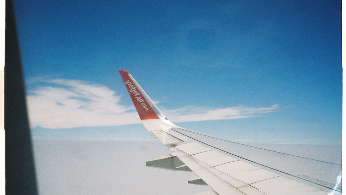 Aerial view from an airplane wing flying over a bright blue sky with scattered clouds.