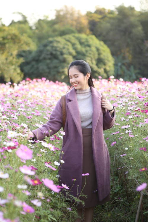 Woman Wearing a Lilac Coat Standing in a Field with Pink Flowers