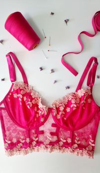 Stylish flat lay of pink lace lingerie with sewing essentials on white background.