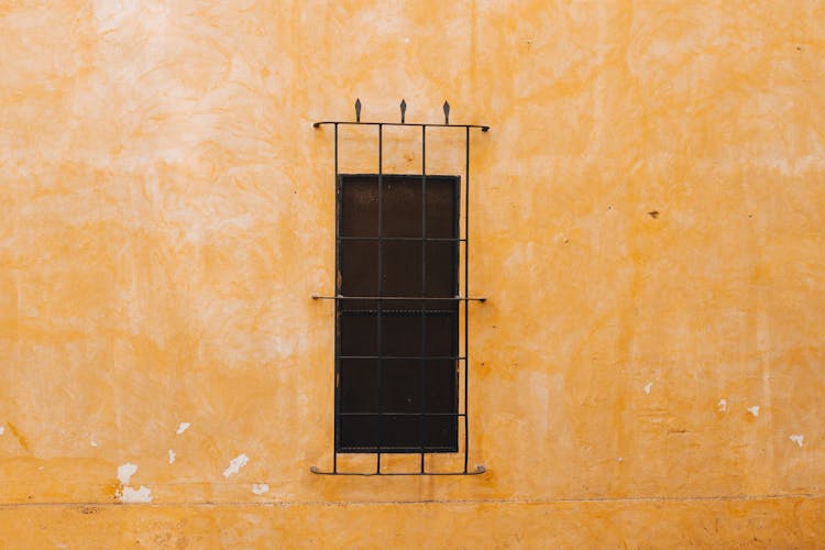 A Window Behind Bars In A Yellow Building 