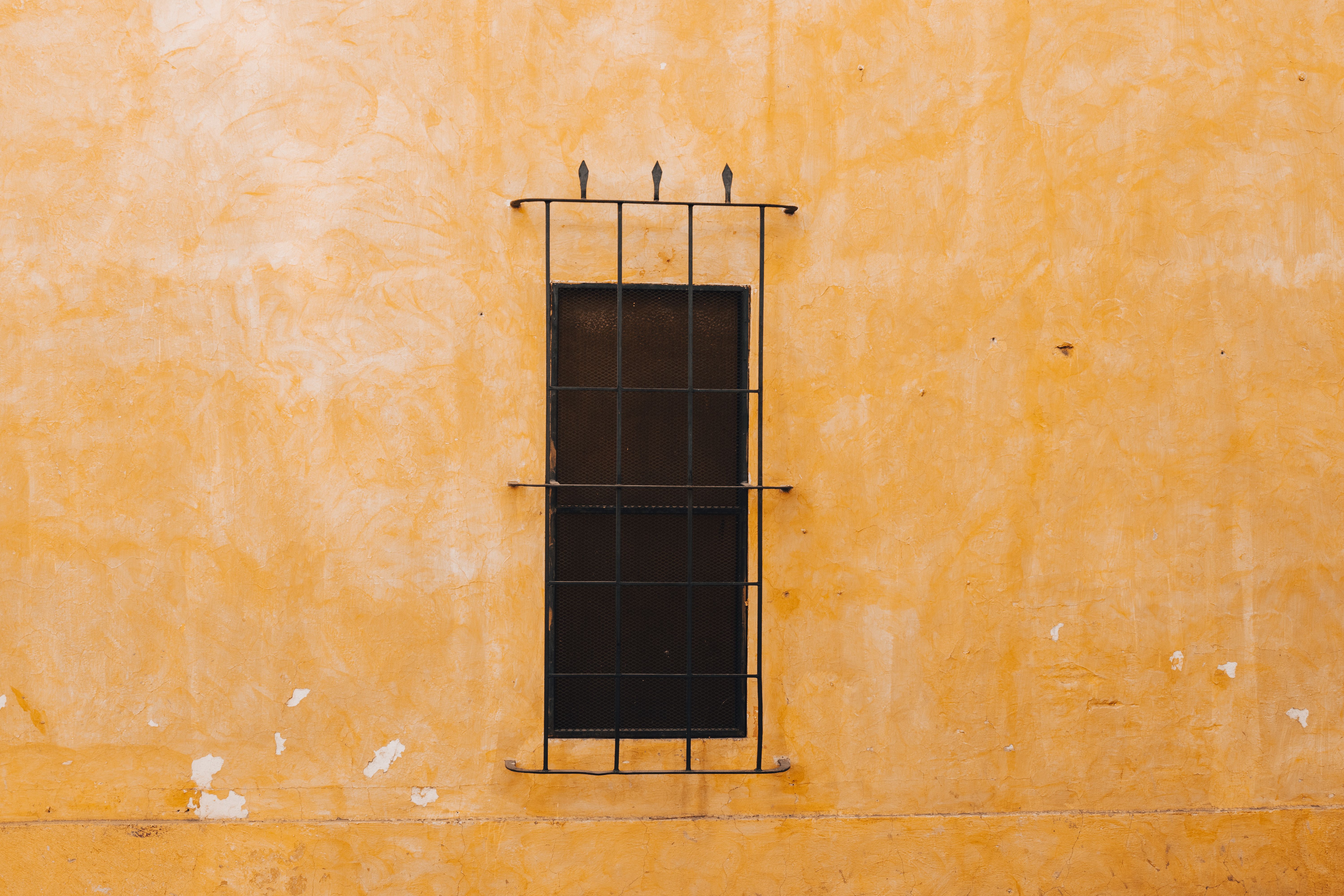 A Window behind Bars in a Yellow Building · Free Stock Photo