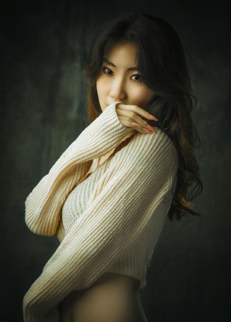 Stylish portrait of a woman in a white sweater, posing gracefully against a gray background.